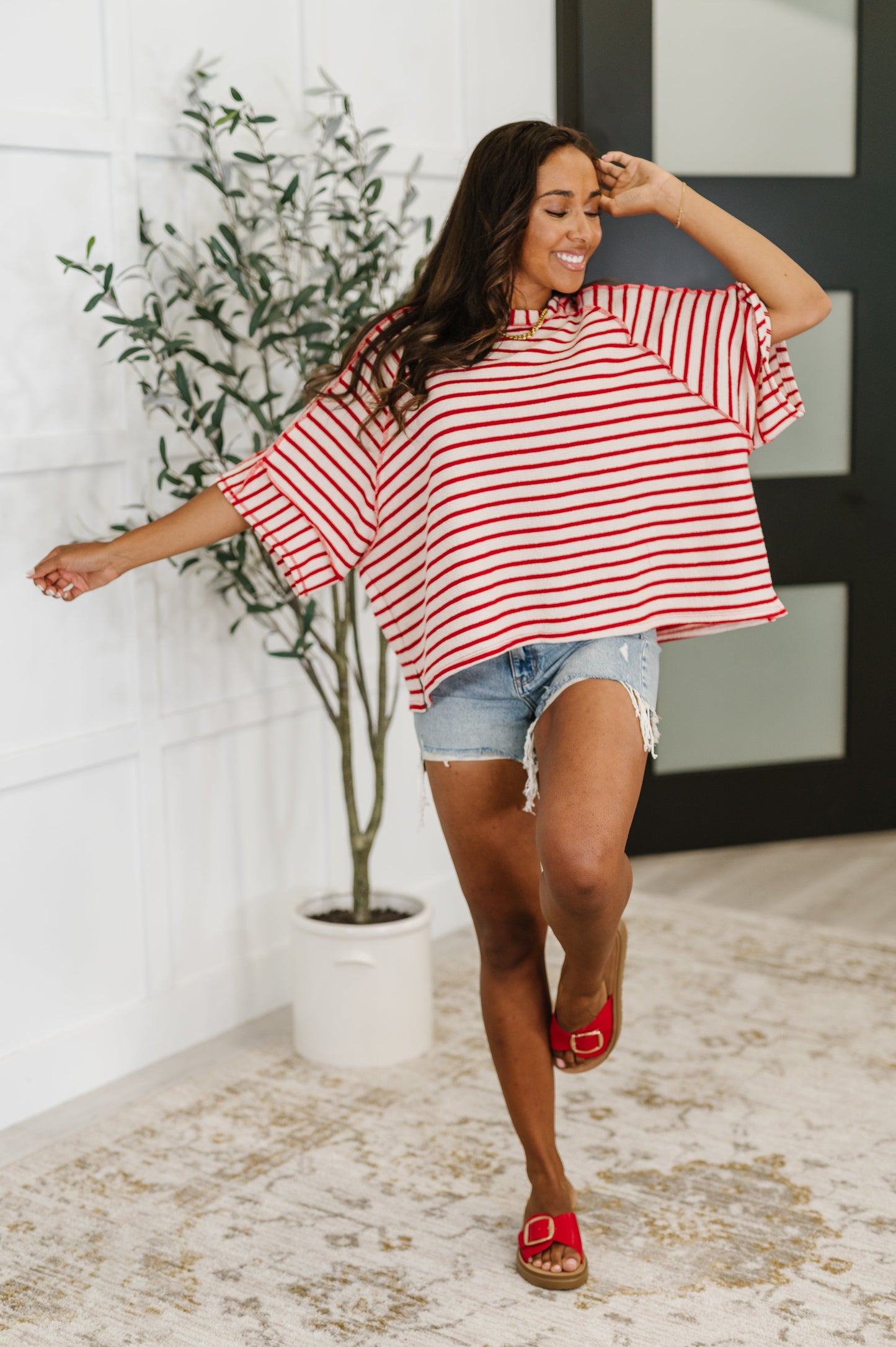 Woman wearing a red and white striped shirt and denim shorts, standing indoors.