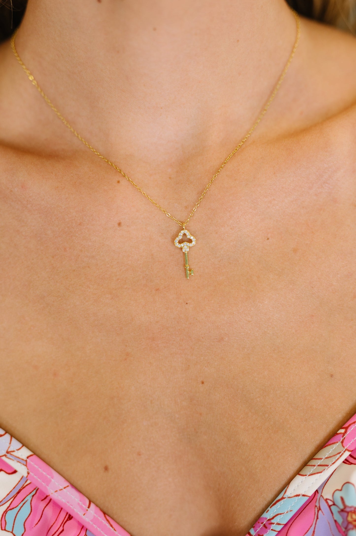 Gold necklace with a key pendant on a person wearing a floral dress.