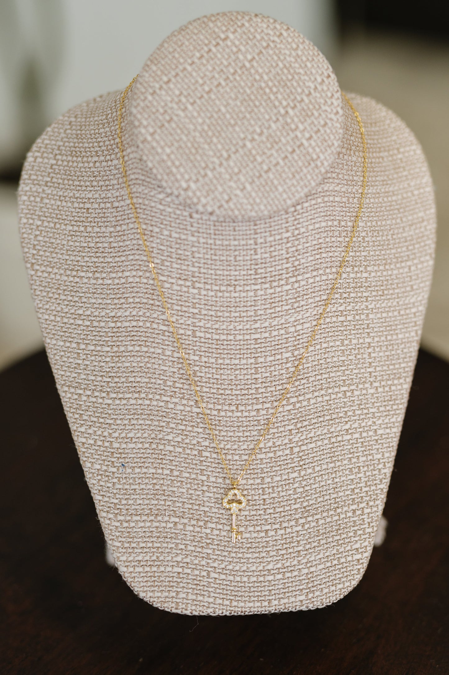 Gold necklace on a gray linen necklace display stand with a blurred background