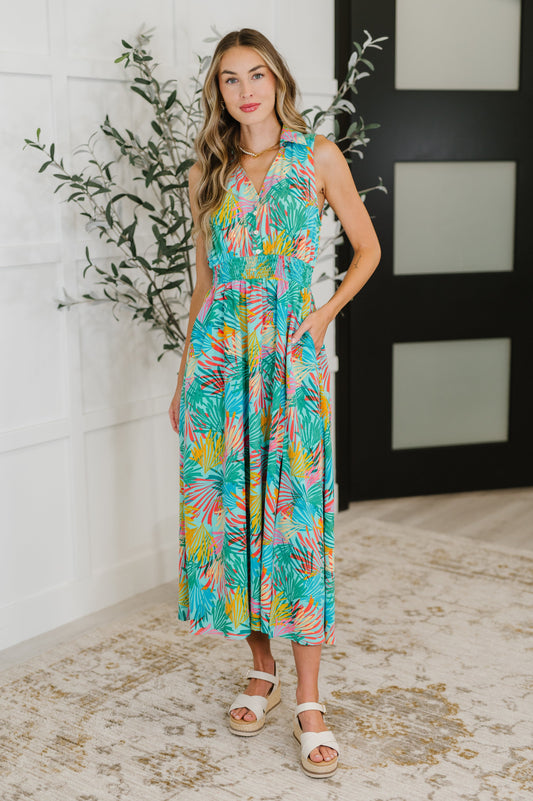 Woman wearing a colorful floral dress standing indoors with a plant in the background