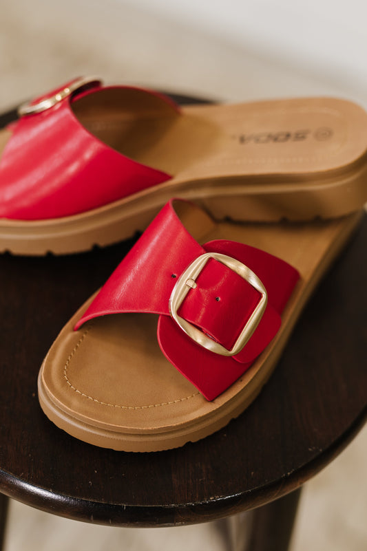 Red faux leather slide sandals with a gold buckle