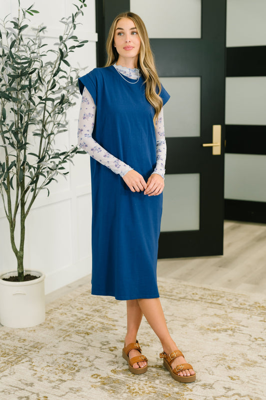 Woman in a blue dress standing indoors with a plant and door in the background