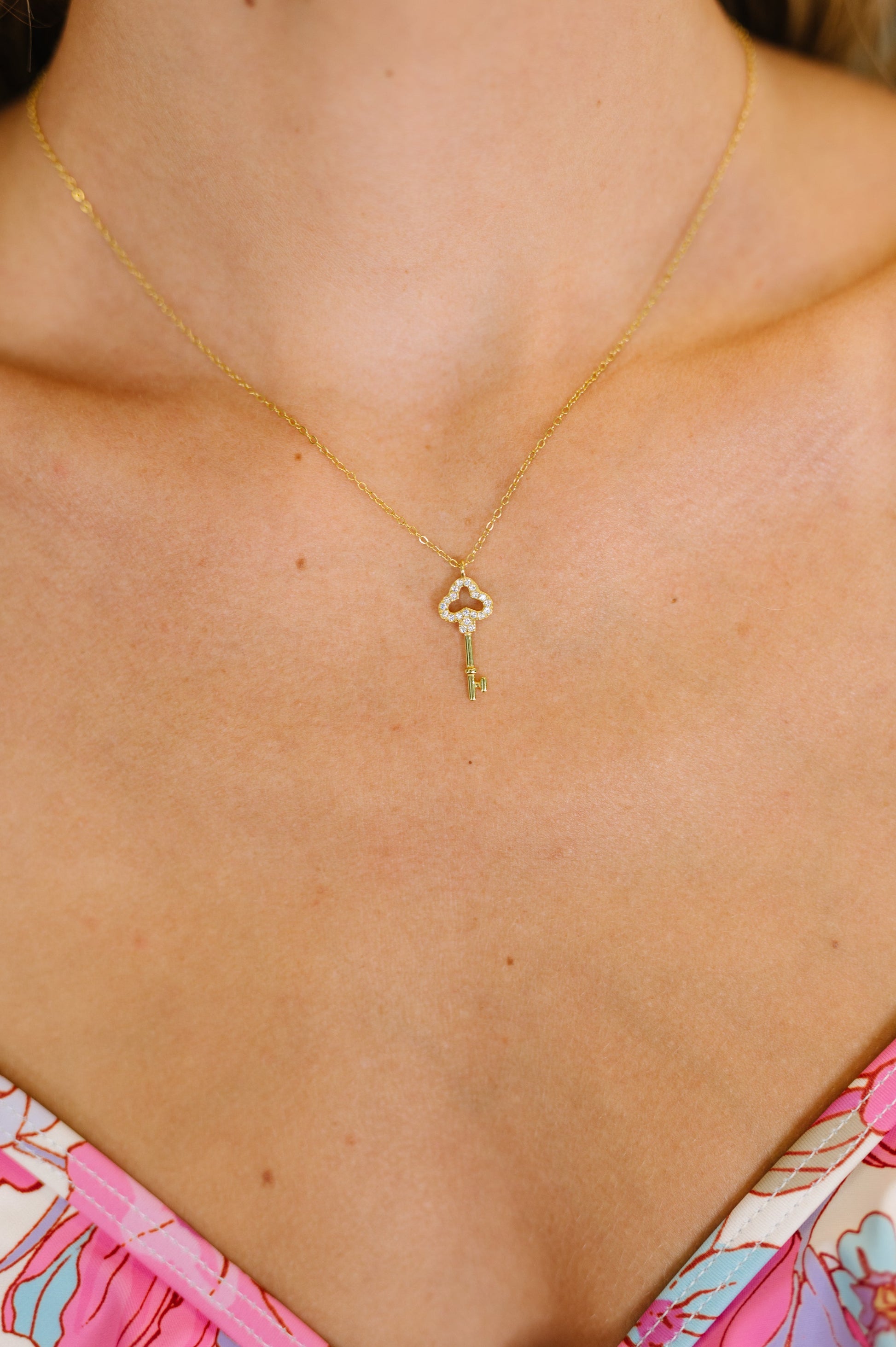 Gold necklace with a key pendant on a person wearing a floral dress.
